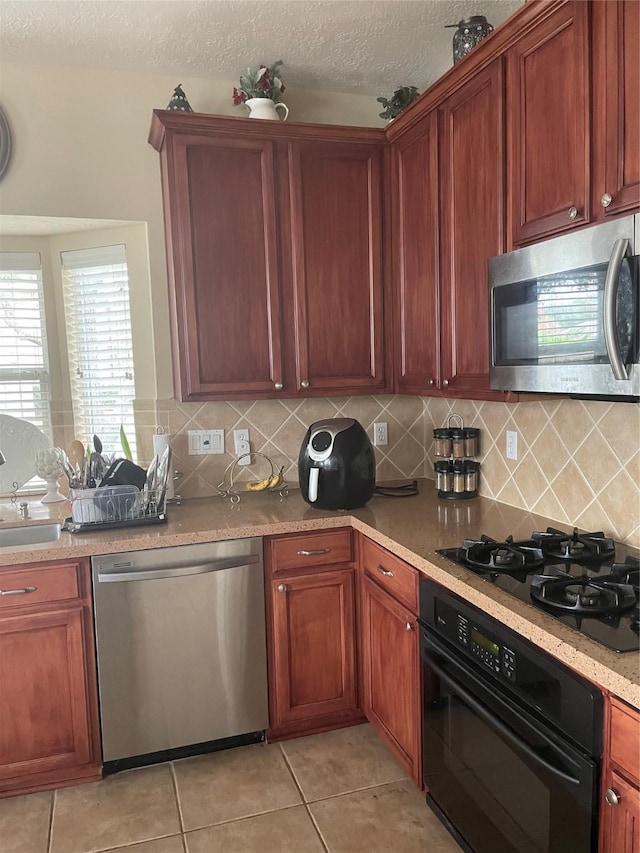 kitchen featuring decorative backsplash, light tile patterned floors, black appliances, and a textured ceiling