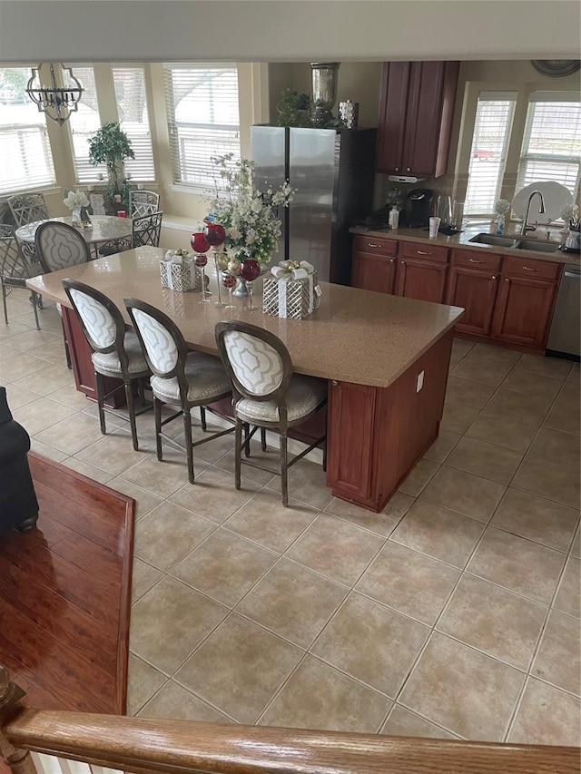 kitchen featuring a center island, sink, light tile patterned floors, appliances with stainless steel finishes, and a notable chandelier