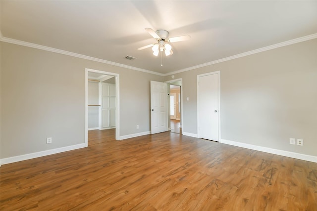 unfurnished bedroom featuring ceiling fan, a spacious closet, ornamental molding, wood-type flooring, and a closet