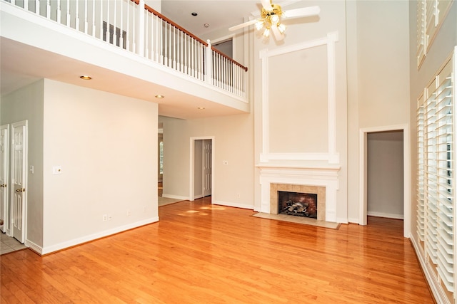 unfurnished living room featuring ceiling fan, a fireplace, a towering ceiling, and light wood-type flooring