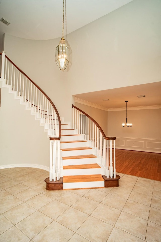 stairs featuring crown molding, a towering ceiling, wood-type flooring, and an inviting chandelier