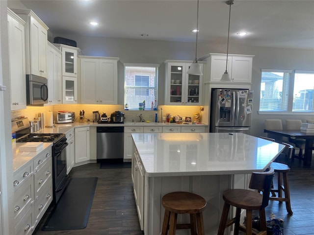 kitchen with white cabinets, stainless steel appliances, a kitchen island, and dark hardwood / wood-style floors