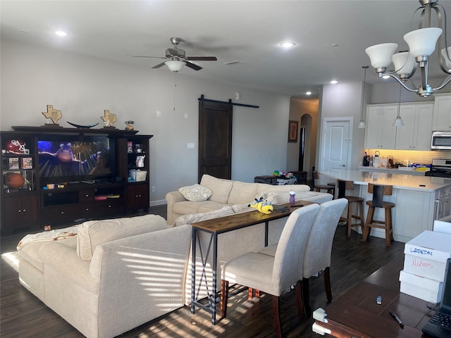 living room featuring ceiling fan with notable chandelier, a barn door, and dark hardwood / wood-style flooring