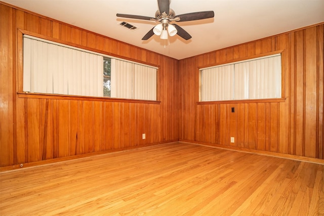 unfurnished room with ceiling fan, wooden walls, and light hardwood / wood-style flooring