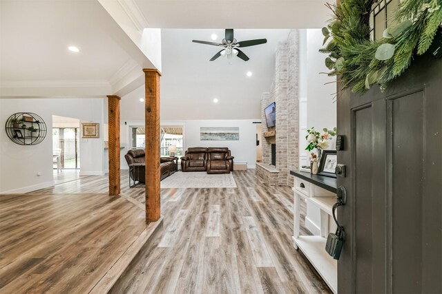 living room featuring ceiling fan, decorative columns, wood-type flooring, a fireplace, and ornamental molding