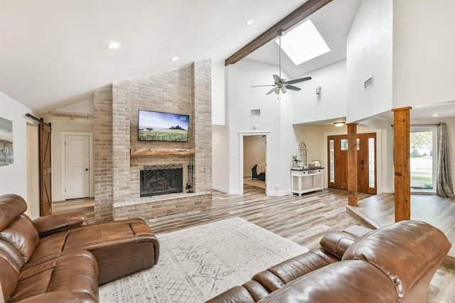 living room with a brick fireplace, a barn door, light hardwood / wood-style flooring, and ceiling fan