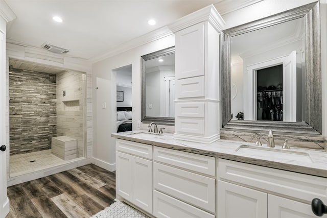 bathroom featuring wood-type flooring, vanity, a tile shower, and crown molding