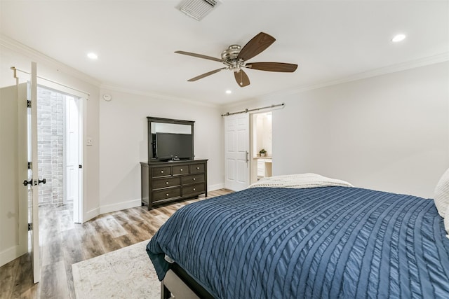 bedroom with light wood-type flooring, ornamental molding, ceiling fan, a barn door, and connected bathroom