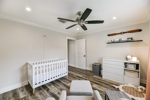 bedroom with ceiling fan, dark hardwood / wood-style floors, a crib, and ornamental molding