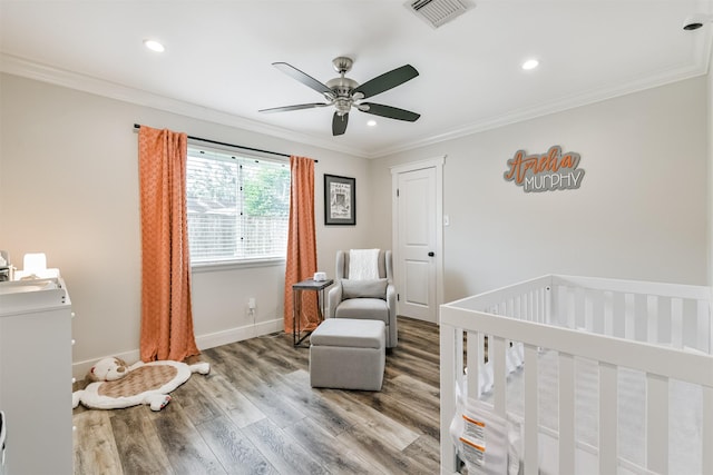 bedroom featuring ceiling fan, hardwood / wood-style flooring, a crib, and ornamental molding