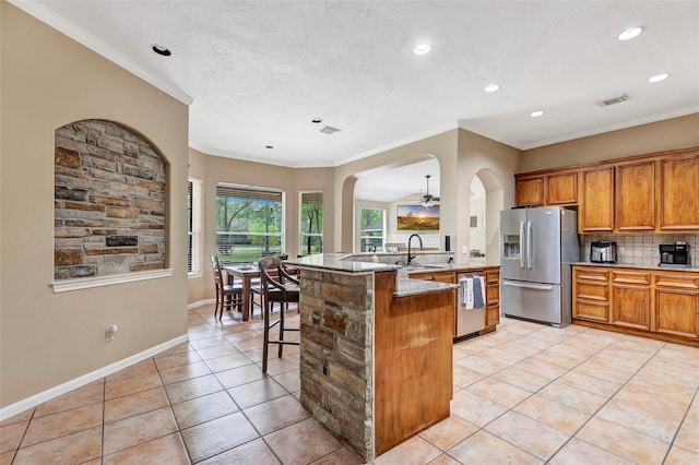 kitchen with decorative backsplash, appliances with stainless steel finishes, a kitchen breakfast bar, ornamental molding, and a center island with sink