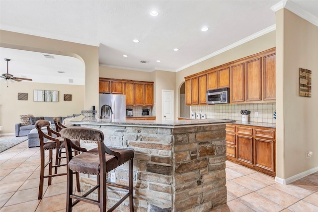 kitchen featuring appliances with stainless steel finishes, a kitchen bar, decorative backsplash, light tile patterned flooring, and ornamental molding