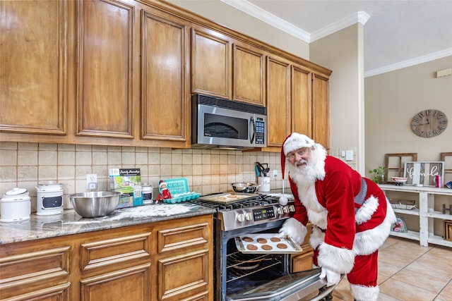 kitchen with appliances with stainless steel finishes, light stone counters, crown molding, and light tile patterned flooring