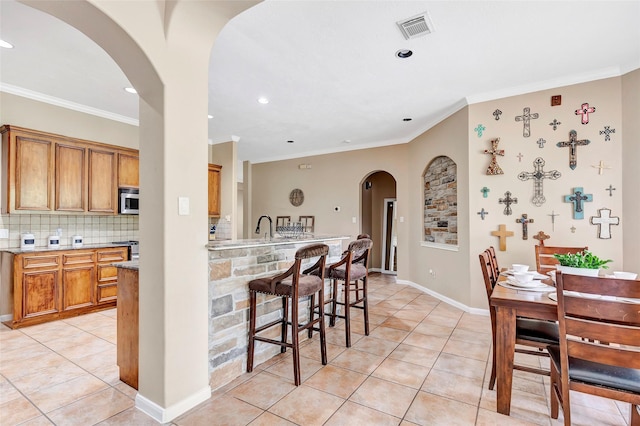 kitchen featuring backsplash, a breakfast bar, crown molding, sink, and light tile patterned flooring