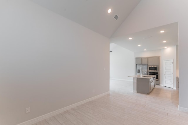 kitchen featuring an island with sink, stainless steel appliances, light wood-type flooring, high vaulted ceiling, and sink