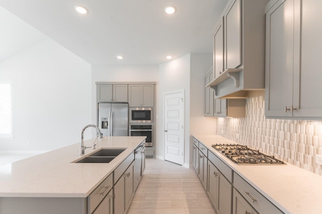 kitchen featuring a center island with sink, gray cabinets, appliances with stainless steel finishes, decorative backsplash, and sink