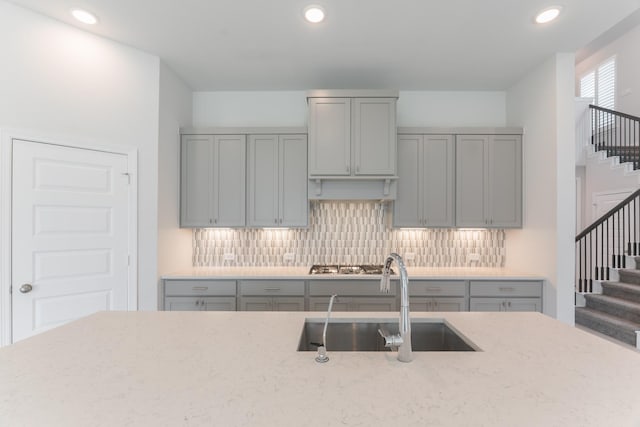 kitchen featuring backsplash, light stone countertops, sink, and gray cabinets