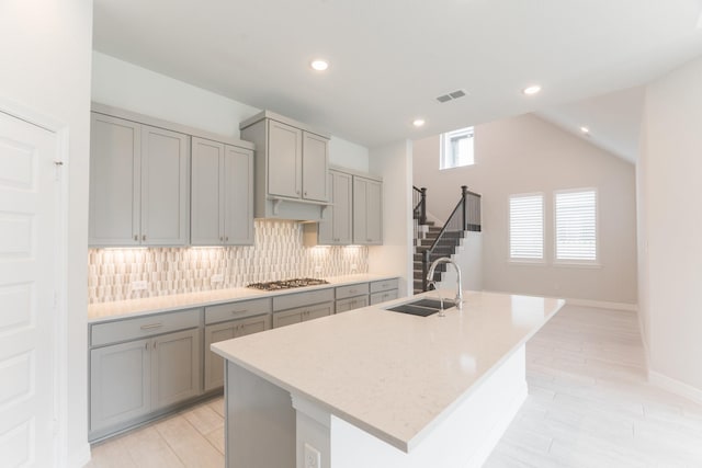 kitchen featuring sink, gray cabinetry, a kitchen island with sink, and stainless steel gas stovetop