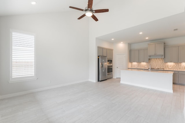 kitchen featuring ceiling fan, backsplash, a kitchen island with sink, appliances with stainless steel finishes, and gray cabinetry