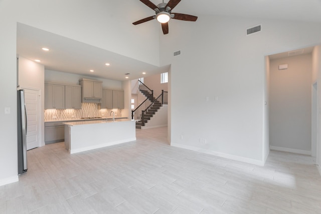 kitchen featuring a center island with sink, ceiling fan, gray cabinetry, backsplash, and stainless steel refrigerator