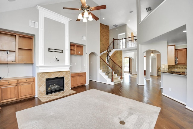 living room with ceiling fan, dark hardwood / wood-style flooring, a tile fireplace, and high vaulted ceiling