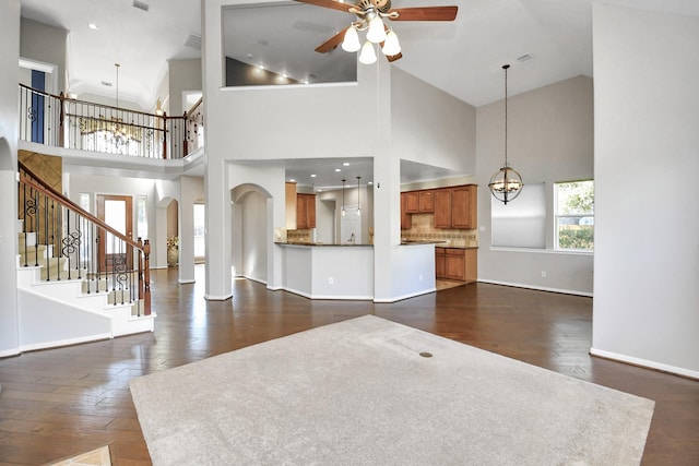 unfurnished living room with ceiling fan with notable chandelier, high vaulted ceiling, and dark hardwood / wood-style floors