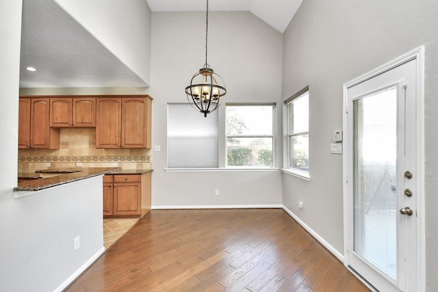 kitchen featuring dark stone counters, decorative light fixtures, light hardwood / wood-style flooring, decorative backsplash, and a notable chandelier