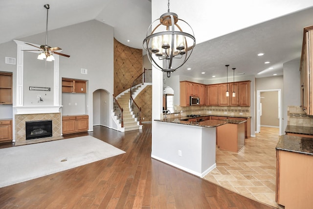 kitchen featuring high vaulted ceiling, a tile fireplace, dark stone counters, light wood-type flooring, and decorative light fixtures