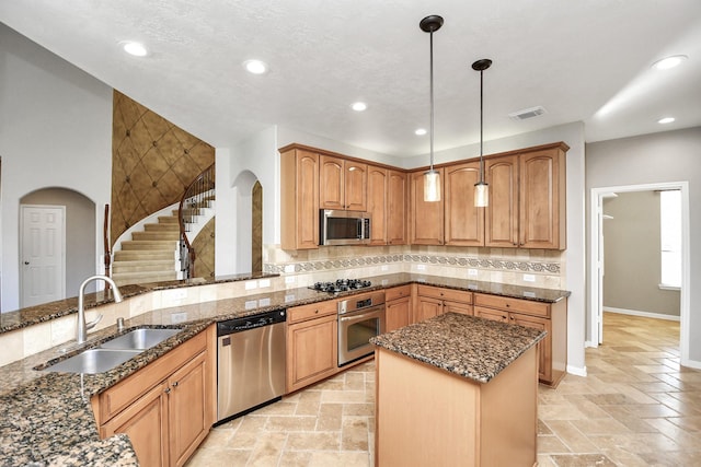 kitchen featuring sink, tasteful backsplash, pendant lighting, dark stone counters, and appliances with stainless steel finishes