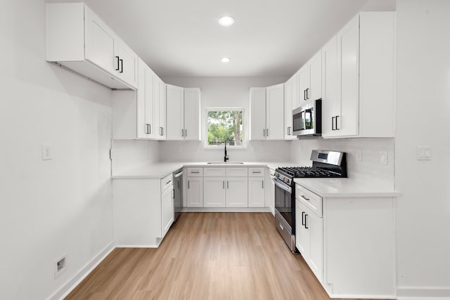 kitchen featuring backsplash, sink, light wood-type flooring, appliances with stainless steel finishes, and white cabinetry