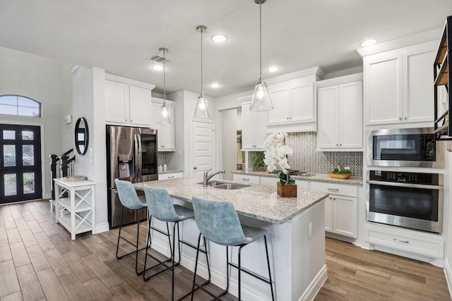 kitchen featuring appliances with stainless steel finishes, sink, decorative light fixtures, white cabinets, and an island with sink