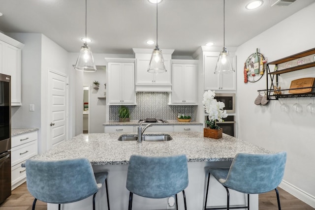 kitchen featuring dark wood-type flooring, sink, decorative light fixtures, white cabinets, and an island with sink