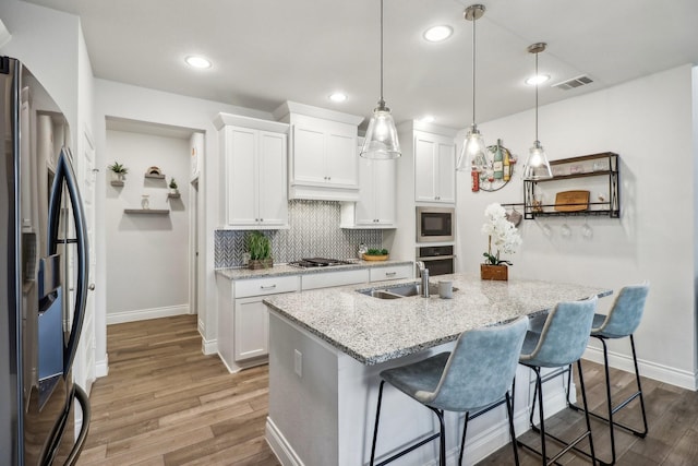 kitchen with light stone countertops, white cabinetry, hanging light fixtures, stainless steel appliances, and a breakfast bar area