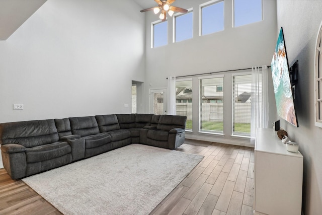 living room featuring ceiling fan, a towering ceiling, and light hardwood / wood-style flooring