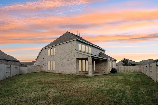 back house at dusk featuring a yard and a patio area