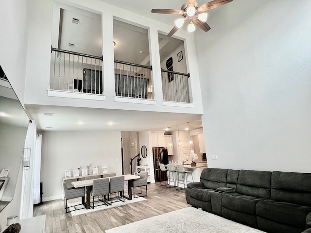 living room featuring light wood-type flooring, a towering ceiling, and ceiling fan