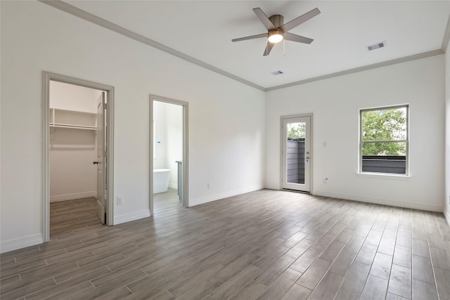 unfurnished bedroom with a walk in closet, ensuite bath, ornamental molding, ceiling fan, and dark wood-type flooring