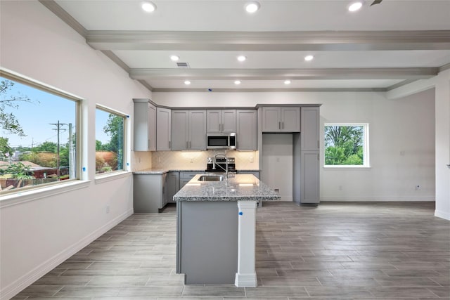 kitchen with gray cabinetry, light stone counters, sink, and a kitchen island with sink