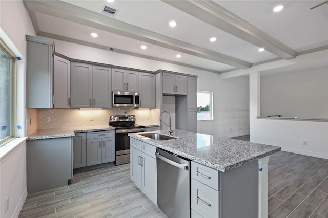 kitchen with light stone countertops, sink, light hardwood / wood-style floors, a kitchen island with sink, and appliances with stainless steel finishes