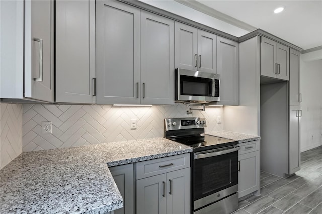 kitchen with light stone countertops, stainless steel appliances, gray cabinets, and tasteful backsplash