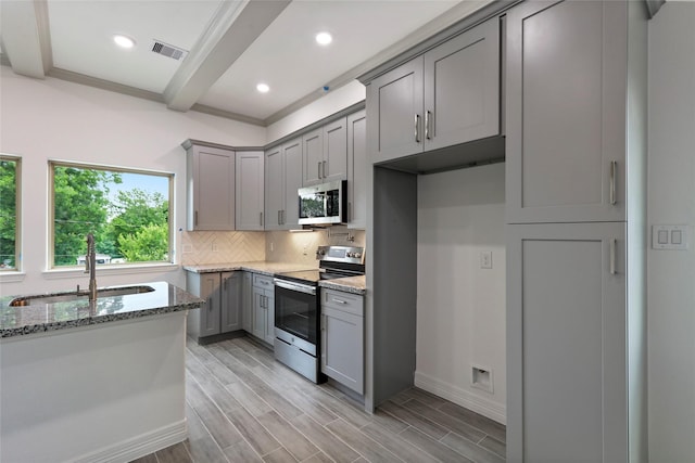 kitchen with sink, gray cabinets, appliances with stainless steel finishes, light hardwood / wood-style floors, and light stone counters