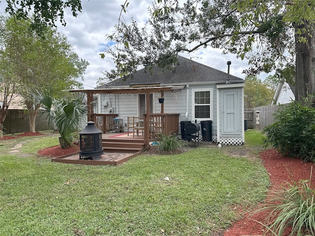 back of house featuring a lawn, a wooden deck, and an outdoor fire pit