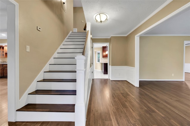 staircase with wood-type flooring, a textured ceiling, and ornamental molding