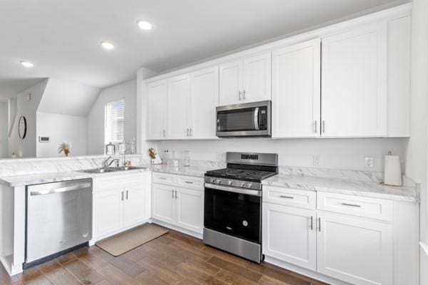 kitchen with white cabinets, vaulted ceiling, appliances with stainless steel finishes, dark hardwood / wood-style flooring, and kitchen peninsula