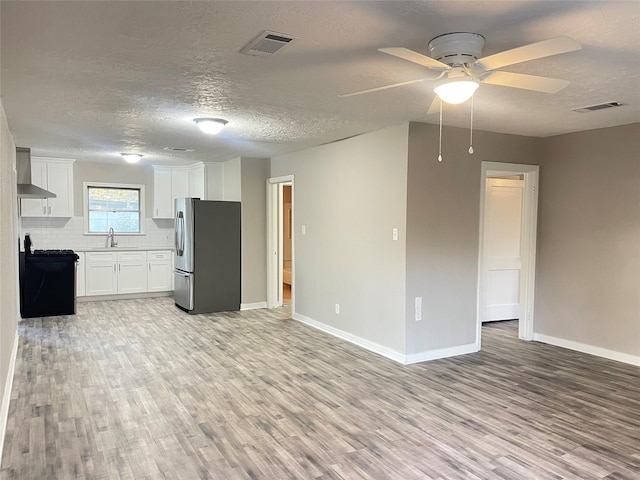 kitchen featuring stainless steel refrigerator, sink, wall chimney exhaust hood, tasteful backsplash, and white cabinets