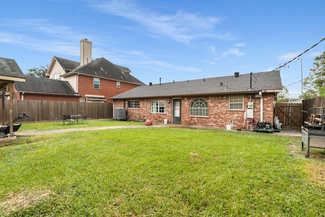 rear view of house with central AC unit and a yard