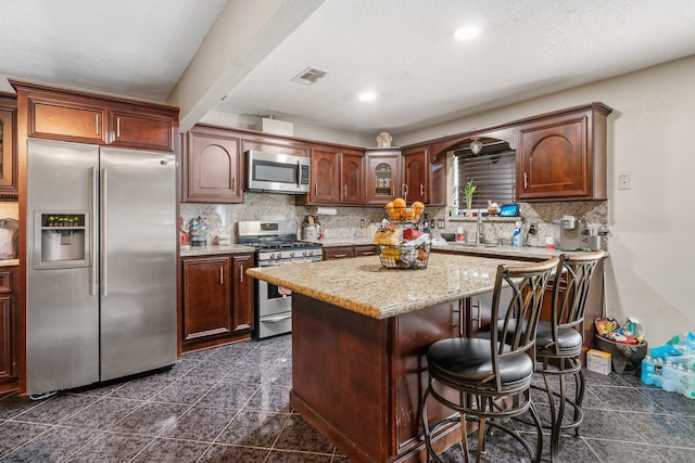 kitchen featuring backsplash, a kitchen island, light stone counters, and stainless steel appliances