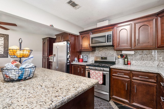 kitchen with light stone countertops, decorative backsplash, stainless steel appliances, and ceiling fan