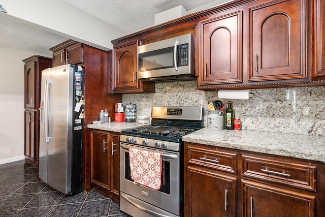 kitchen featuring appliances with stainless steel finishes, tasteful backsplash, light stone counters, a textured ceiling, and dark tile patterned floors