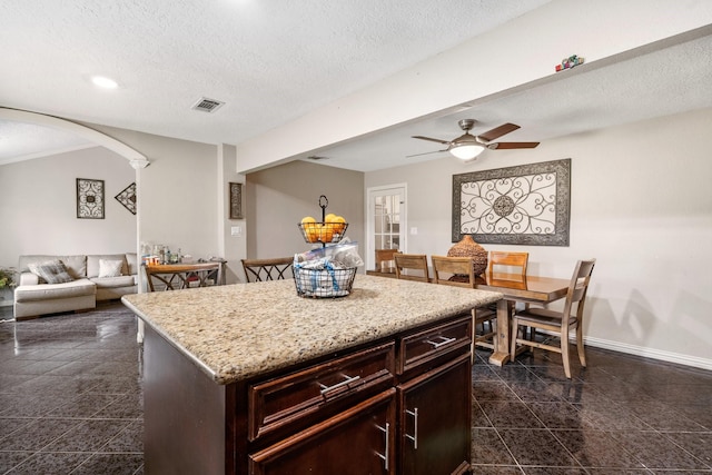 kitchen featuring ceiling fan, a kitchen island, light stone countertops, and a textured ceiling